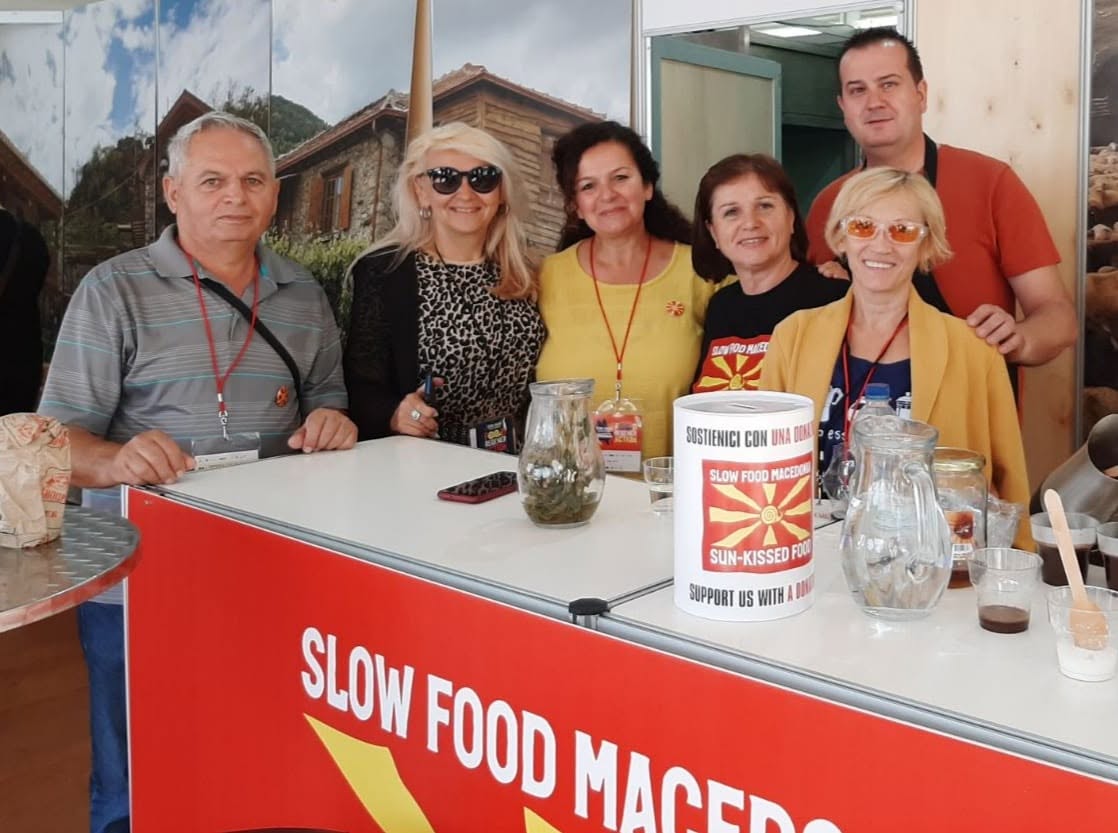 Шест посетители стојат зад пулт со натпис Slow Food Macedonia.