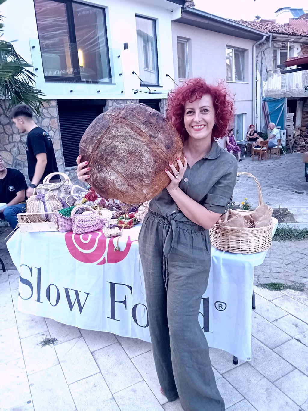 Насмеана жена држи голем тркалезен леб пред маса на Slow Food.
